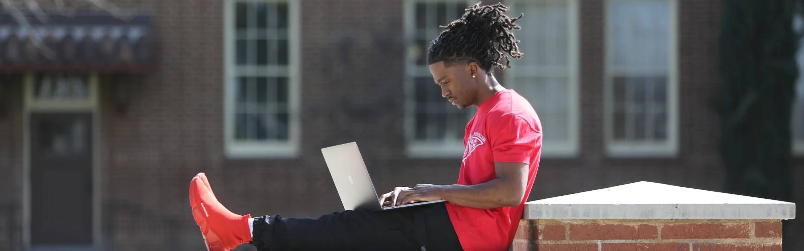 black student sitting in front of library on laptop