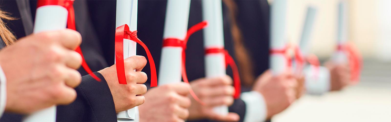 Scrolls of diplomas in the hands of a group of graduates. 